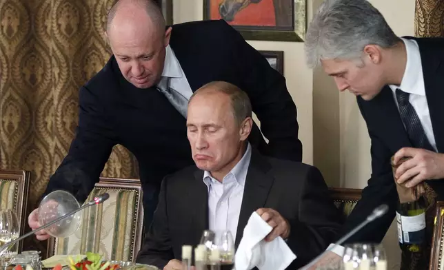 FILE - Businessman Yevgeny Prigozhin, left, serves a meal to Russian Prime Minister Vladimir Putin, center, at a restaurant outside Moscow, Russia, on Nov. 11, 2011. Prigozhin, an ex-convict, owned a restaurant in St. Petersburg where the Russian leader took foreign leaders, earning him the nickname of "Putin's chef." He won lucrative catering contracts and later started a private military company. (AP Photo/Misha Japaridze, Pool, File)