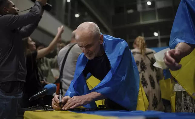 Valeriy Matiushenko, who spent over seven years in Russian captivity, signs the Ukrainian national flag in Kyiv airport, Ukraine, Saturday, June 29, 2024. Ten Ukrainians who had been held prisoners for years, were released from Russian captivity on Friday with a mediation of Vatican, said Ukraine's President Volodymyr Zelenskyy. (AP Photo/Alex Babenko)