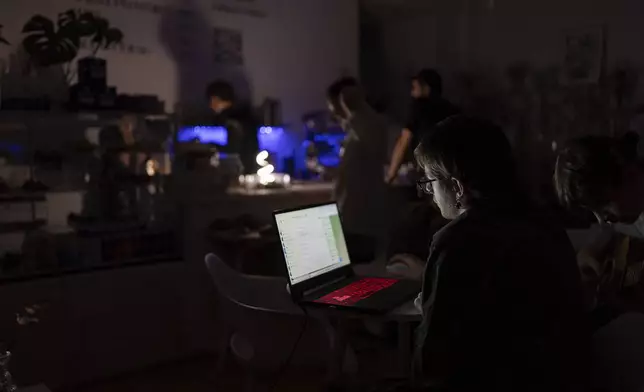 A man is working on his laptop at a coffee shop, which operates during blackouts in Kyiv, Ukraine, Friday, June 7, 2024. Ukraine is experiencing rolling blackouts as Russia intensified strikes targeting energy infrastructure over the past three months. (AP Photo/Alex Babenko)