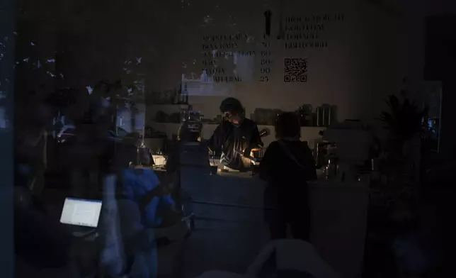 A barman is seen working through the window of a coffee shop during power cuts in Kyiv, Ukraine, Friday, June 7, 2024. Ukraine, including Kyiv, is struggling to cope with a new wave of rolling blackouts after relentless Russian attacks took out half the country’s power generation capacity. (AP Photo/Alex Babenko)