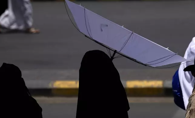 A woman holds an umbrella to protect herself from the sun as she leaves after offering prayers outside at the Grand Mosque, during during the annual Hajj pilgrimage in Mecca, Saudi Arabia, Thursday, June 13, 2024. Hajj is the annual Islamic pilgrimage to Mecca in Saudi Arabia that is required once in a lifetime of every Muslim who can afford it and is physically able to make it. Some Muslims make the journey more than once. (AP Photo/Rafiq Maqbool)