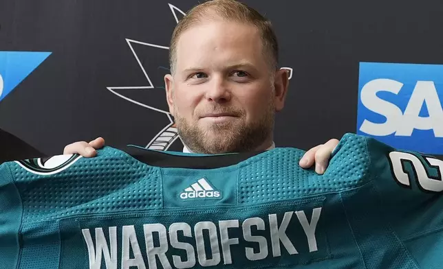 Ryan Warsofsky holds up a jersey at a news conference where he was introduced as the NHL hockey head coach of the San Jose Sharks in San Jose, Calif., Monday, June 17, 2024. (AP Photo/Jeff Chiu)