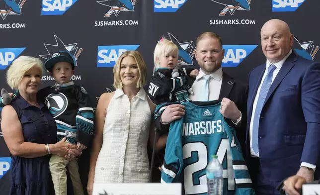 Ryan Warsofsky, second from right, holds a jersey as he poses for photos with his family at a news conference where he was introduced as the NHL hockey head coach of the San Jose Sharks in San Jose, Calif., Monday, June 17, 2024. (AP Photo/Jeff Chiu)