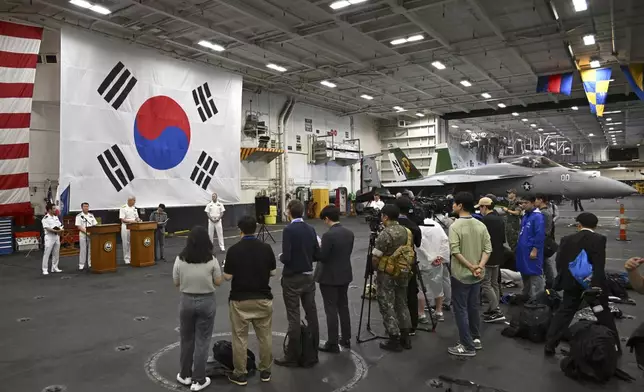 Crew members and member of the media gather in the hanger of the Theodore Roosevelt (CVN 71), a nuclear-powered aircraft carrier, anchored in Busan Naval Base in Busan, South Korea Saturday, June 22, 2024. (Song Kyung-Seok/Pool Photo via AP)