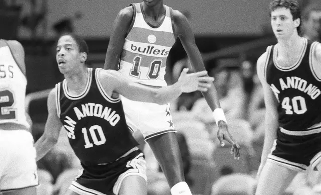 FILE - Washington Bullets center Manute Bol towers over opponents and teammates during the team's NBA basketball game against the San Antonio Spurs in New York, Oct. 17, 1985. Just 13 years after South Sudan emerged from civil war to become an independent nation in 2011, it will mark a milestone next month when the world’s youngest nation makes its Olympic basketball debut. Bol introduced Luol Deng to basketball. (AP Photo/G. Paul Burnett, File)