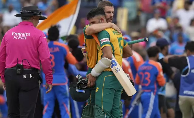 South Africa's Anrich Nortje consoles teammate Keshav Maharaj as India's players celebrate their win against South Africa in the ICC Men's T20 World Cup final cricket match at Kensington Oval in Bridgetown, Barbados, Saturday, June 29, 2024. (AP Photo/Ramon Espinosa)