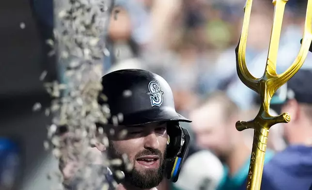 Seattle Mariners' Mitch Haniger braces for a bag of seeds thrown at him by a teammate as he holds a trident to celebrate hitting a solo home run against the Minnesota Twins during the third inning of a baseball game Saturday, June 29, 2024, in Seattle. (AP Photo/Lindsey Wasson)