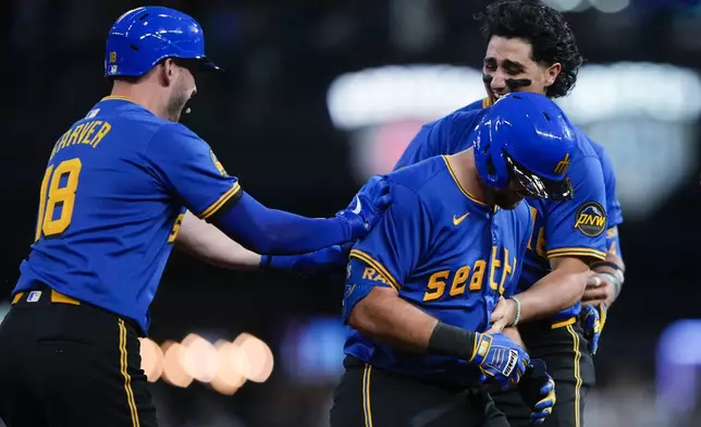 Seattle Mariners' Cal Raleigh, center, is greeted by Mitch Garver (18) and Josh Rojas, right, after hitting a ground ball to drive in the winning run in the 10th inning against the Minnesota Twins in a baseball game Friday, June 28, 2024, in Seattle. The Mariners won 3-2. (AP Photo/Lindsey Wasson)