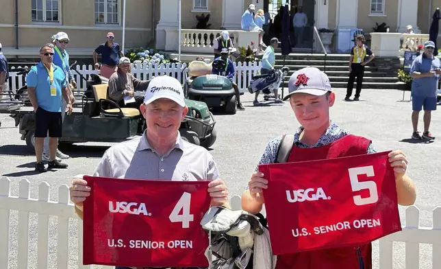 Frank Bensel, left, and his caddie and 14-year-old son, Hagen, pose with hole 4 and 5 flags after Bensel turned up a pair of aces on the back-to-back holes during the second round of the U.S. Senior Open golf tournament in Newport, R.I., Friday, June 28, 2024. (AP Photo/Jimmy Golen)