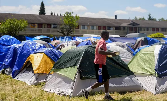 A man transports food donated by community members at an encampment of asylum-seekers mostly from Venezuela, Congo and Angola next to an unused motel owned by the county, Wednesday, June 5, 2024, in Kent, Washington. The group of about 240 asylum-seekers is asking to use the motel as temporary housing while they look for jobs and longer-term accommodations. (AP Photo/Lindsey Wasson)