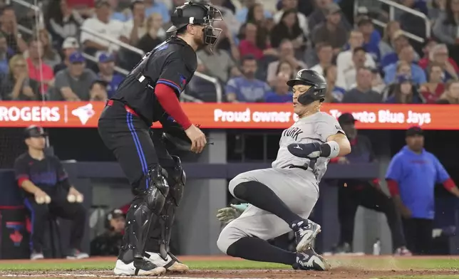 New York Yankees' Aaron Judge scores next to Toronto Blue Jays catcher Danny Jansen on an RBI double by J.D. Davis during the sixth inning of a baseball game Friday, June 28, 2024, in Toronto. (Chris Young/The Canadian Press via AP)