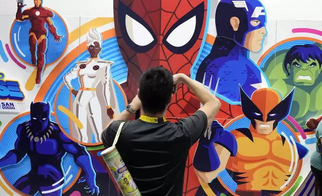 An attendee takes a picture of an illustrated wall of Marvel superhero characters during preview night for Comic-Con International, Wednesday, July 24, 2024, in San Diego. (AP Photo/Chris Pizzello)