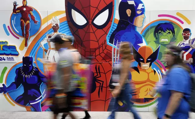 Convention attendees blur past a wall of illustrated Marvel superhero characters during preview night for Comic-Con International, Wednesday, July 24, 2024, in San Diego. (AP Photo/Chris Pizzello)