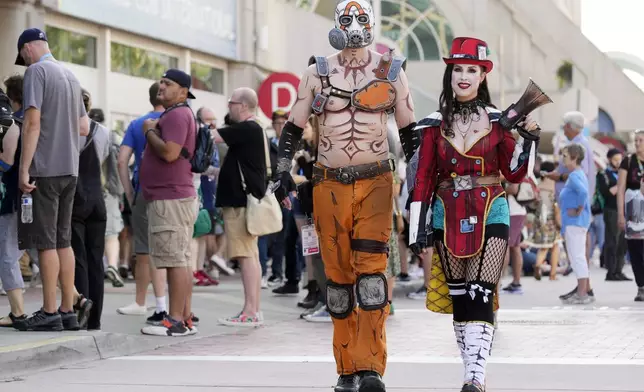 Chris Lane, left, dressed as Krieg from the upcoming movie "Borderlands," and his wife Sharon, dressed as Mad Moxxi, walk past attendees before preview night for Comic-Con International, Wednesday, July 24, 2024, in San Diego. (AP Photo/Chris Pizzello)