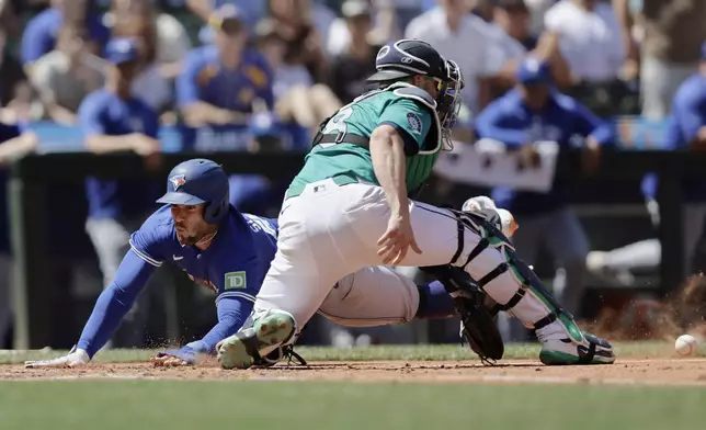 Toronto Blue Jays' George Springer scores before the tag from Seattle Mariners catcher Mitch Garver during the fifth inning in a baseball game, Saturday, July 6, 2024, in Seattle. (AP Photo/John Froschauer)