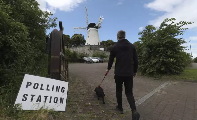 A man and his dog walk towards Falwell windmill and mill which is a temporary polling station in Sunderland, England, Thursday, July 4, 2024.Britain goes to the polls Thursday after Prime Minister Rishi Sunak called a general election. (AP Photo/Scott Heppell)
