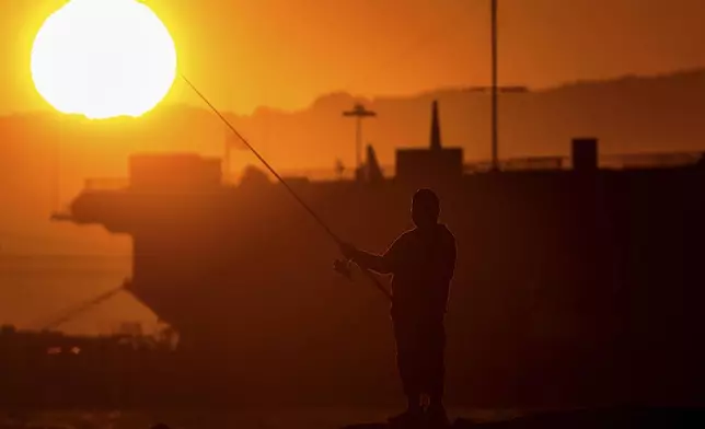A man fishes off a jetty in Alameda, Calif., as the sun sets over the San Francisco Bay on Monday, July 1, 2024. An extended heatwave predicted to blanket Northern California has resulted in red flag fire warnings and the possibility of power shutoffs beginning Tuesday. (AP Photo/Noah Berger)