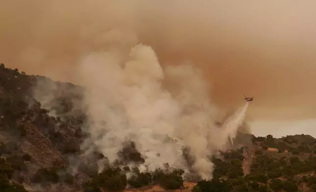 A water-dropping helicopter drops on flames from the advancing Lake Fire in Los Olivos, Calif., Saturday, July 6, 2024. (AP Photo/Eric Thayer)