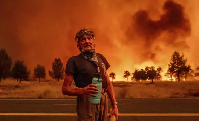 Grant Douglas pauses to drink water while evacuating as the Park Fire jumps Highway 36 near Paynes Creek in Tehama County, Calif., Friday, July 26, 2024. (AP Photo/Noah Berger)