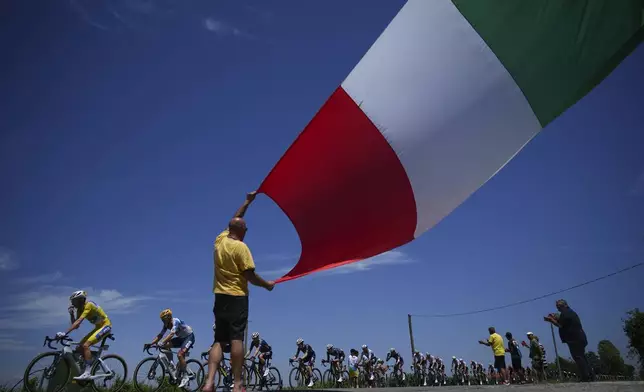 A cycling fan waves the Italian flag as the pack with France's Romain Bardet, wearing the overall leader's yellow jersey, left, passes during the second stage of the Tour de France cycling race over 199.2 kilometers (123.8 miles) with start in Cesenatico and finish in Bologna, Italy, Sunday, June 30, 2024. (AP Photo/Daniel Cole)