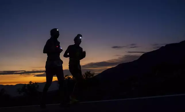 A runner and their pacer run as the sun rises behind them on California Route 190 during the Badwater 135 mile (217 kilometer) ultramarathon in Death Valley, Calif., Tuesday, July 23, 2024. (AP Photo/Ty ONeil)