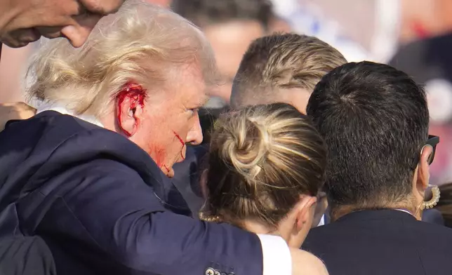 Republican presidential candidate former President Donald Trump is surrounded by U.S. Secret Service agents as he is helped off the stage at a campaign rally in Butler, Pa., Saturday, July 13, 2024. (AP Photo/Gene J. Puskar)