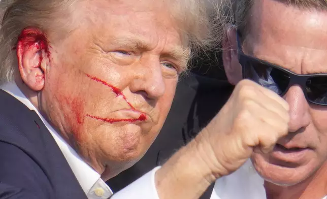 Republican presidential candidate former President Donald Trump gestures while surrounded by U.S. Secret Service agents as he is helped off the stage at a campaign rally in Butler, Pa., Saturday, July 13, 2024. (AP Photo/Gene J. Puskar)