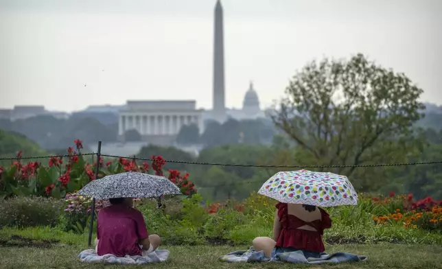 People sit under umbrellas during a rain shower at the Netherlands Carillon on Thursday, July 4, 2024 in Arlington, Va., ahead of a fireworks display at the National Mall in Washington. (AP Photo/Mark Schiefelbein)