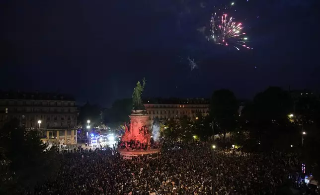 Fireworks go off as people stand in Republique Plaza and react to the projection of results during the second round of the legislative elections, in Paris, France, Sunday, July 7, 2024. Polls have closed in France, and polling projections say a coalition on the left that came together unexpectedly has won the most parliamentary seats in the pivotal runoff elections after a high turnout among voters. Banner at center reads "France is the fabric of migratation." (AP Photo/Christophe Ena)