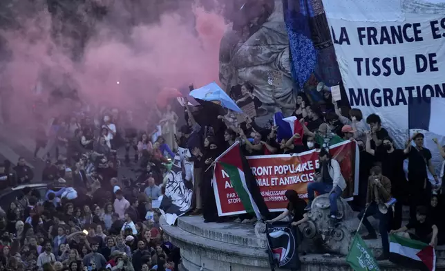 People stand in Republique Plaza as they react to the projection of results during the second round of the legislative elections, in Paris, France, Sunday, July 7, 2024. Polls have closed in France, and polling projections say a coalition on the left that came together unexpectedly has won the most parliamentary seats in the pivotal runoff elections after a high turnout among voters. Banner at center reads "France is the fabric of migratation." (AP Photo/Christophe Ena)