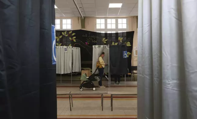 A woman makes her choice in a voting booth during the second round of the legislative elections, Sunday, July 7, 2024 in Paris. France votes Sunday in pivotal runoff elections that could hand a historic victory to Marine Le Pen's far-right National Rally and its inward-looking, anti-immigrant vision — or produce a hung parliament and years of political deadlock. (AP Photo/Aurelien Morissard)