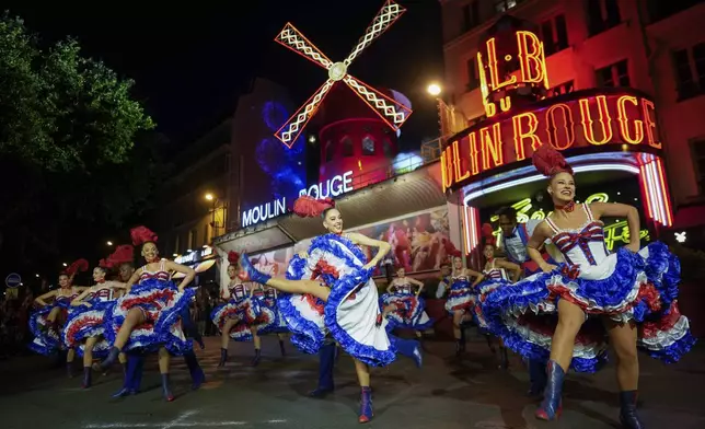 Dancers perform in front of the Moulin Rouge cabaret during the inauguration of the theatre's windmill in Paris, Friday, July 5, 2024. The mill's huge sails inexplicably collapsed after a show last month at the iconic venue, an emblem of the surrounding Montmartre neighborhood and bohemian Paris lifestyle. (AP Photo/Thibault Camus)