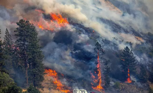 A vehicle drives past the spreading River Fire Thursday, July 25, 2024, near Myrtle, Idaho, before U.S. Highway 12 was closed. Lightning strikes have sparked fast-moving wildfires in Idaho, prompting the evacuation of multiple communities. (August Frank/Lewiston Tribune via AP)