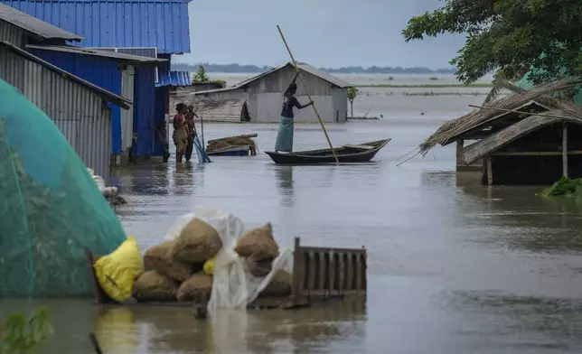 A person rows a country boat as women stand in the flood water near their submerged houses in Morigaon district in the northeastern Indian state of Assam, India, Wednesday, July 3, 2024. (AP Photo/Anupam Nath)