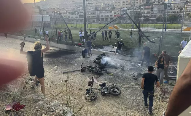 Residents rush to help injured children moments after a rocket attack hit a soccer field in the Druze town of Majdal Shams in the Israeli-controlled Golan Heights, Saturday, July 27, 2024. (AP Photo/Hassan Shams)