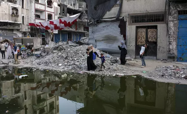 Palestinians displaced by the Israeli air and ground offensive on the Gaza Strip walk next a dark streak of sewage flowing into the streets of the southern town of Khan Younis, Gaza Strip, Thursday, July 4, 2024. (AP Photo/Jehad Alshrafi)