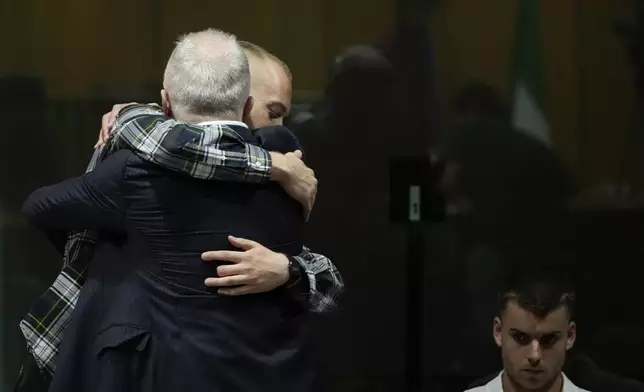 Ethan Elder, left, back to camera, father of Finnegan Lee Elder, hugs his son before the reading of the judgment at the end of a hearing for the appeals trial in which Finnegan is facing murder charges for killing Italian Carabinieri paramilitary police officer Mario Cerciello Rega, in Rome, Wednesday, July 3, 2024. At right sits Gabriel Natale Hjorth charged for the same killing. (AP Photo/ Alessandra Tarantino)