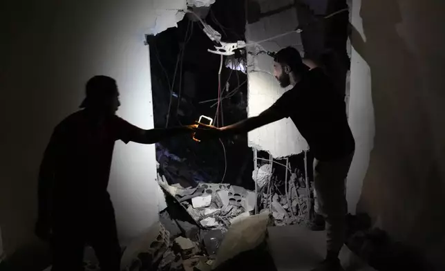 Two men use their phone light, as they check a house on a destroyed building that was hit by an Israeli airstrike in the southern suburbs of Beirut, Lebanon, Tuesday, July 30, 2024. An Israeli airstrike hit Hezbollah's stronghold south of Beirut Tuesday evening causing damage, a Hezbollah official and the group's TV station said.(AP Photo/Hussein Malla)