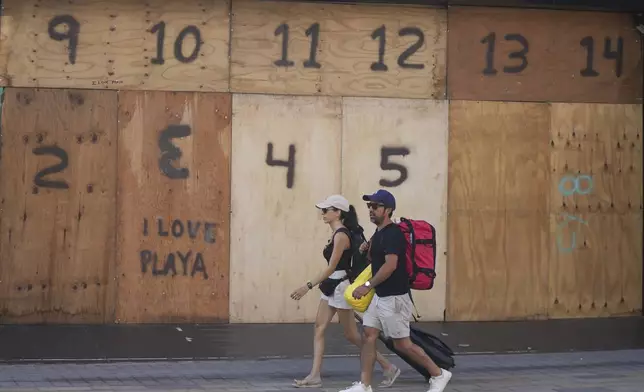 People walk past a souvenir shop's storefront boarded up preparation for the arrival of Hurricane Beryl, in Playa del Carmen, Mexico, Thursday, July 4, 2024. (AP Photo/Fernando Llano)
