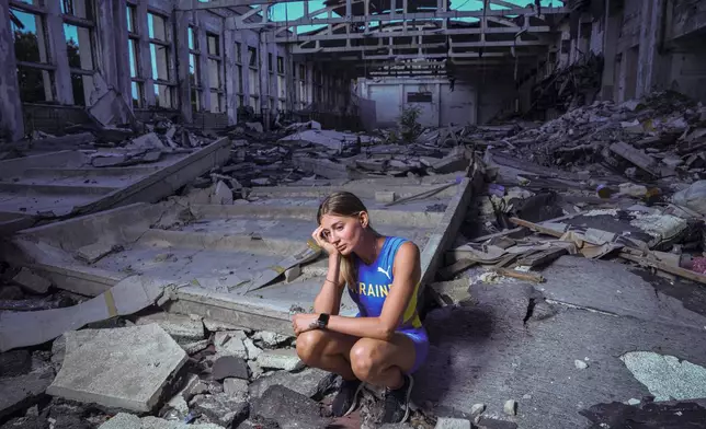 Kateryna Tabashnyk, a high jumper, sits for a portrait Sunday, June 9, 2024, at the athletics arena of the "Polytechnic" sports complex, which was destroyed by a Russian rocket attack, in Kharkiv, Ukraine. On the eve of the war, which started Feb. 24, 2022, Ukraine cancelled its athletics championship and Tabashnyk was in Kharkiv. The threat posed by thousands of Russian troops at the border, just 20 kilometers (12 miles) from her hometown, was real. But Tabashnyk said, “I was 100% sure that this could not happen.” (AP Photo/Evgeniy Maloletka)