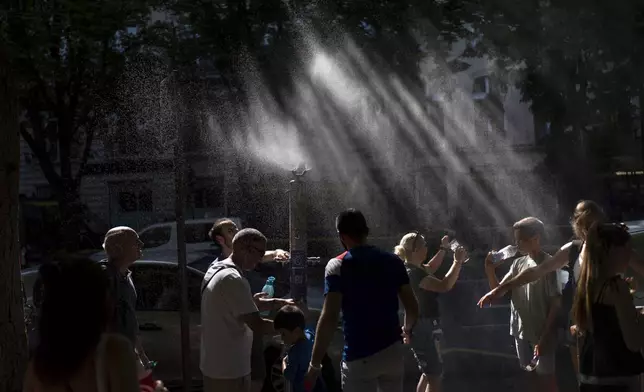 People cool off under a misting fountain while filling their water bottles on a hot afternoon during the 2024 Summer Olympics, Monday, July 29, 2024, in Paris. (AP Photo/David Goldman)