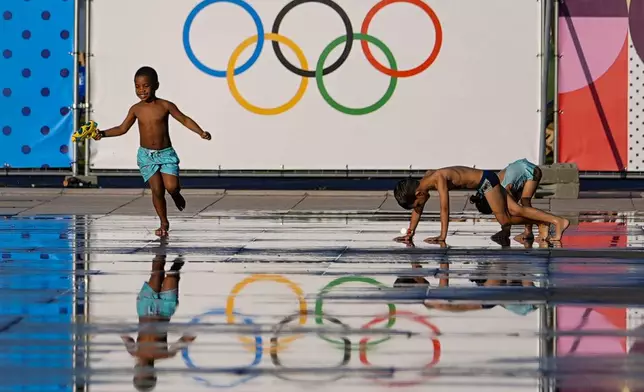 Children play at a splash fountain area near signage for the 2024 Summer Olympics, Tuesday, July 23, 2024, in Nice, France. Nice will host six soccer matches during the summer games. (AP Photo/Julio Cortez)