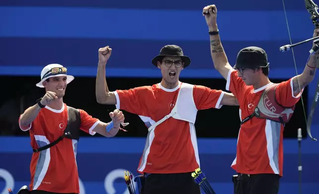 Turkey's Mete Gazoz, right, Berkim Tumer, left, and Turkey's Abdullah Yildirmis celebrate a win during the men's team quarterfinals Archery competition against India at the 2024 Summer Olympics, Monday, July 29, 2024, in Paris, France. (AP Photo/Rebecca Blackwell)