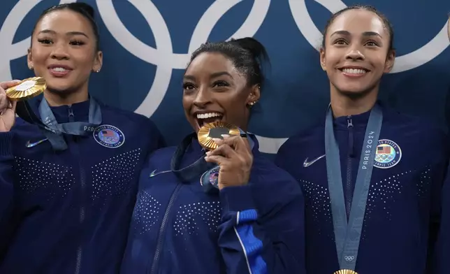 From left to right, Suni Lee, Simone Biles, Hezly Rivera celebrate after winning the gold medal during the women's artistic gymnastics team finals round at Bercy Arena at the 2024 Summer Olympics, Tuesday, July 30, 2024, in Paris, France. (AP Photo/Charlie Riedel)