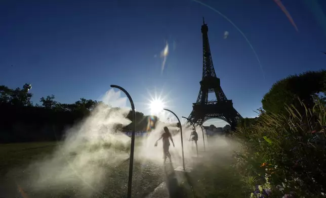 A spectator walks through a water mist sprayers on her way to Eiffel Tower Stadium to watch a beach volleyball at the 2024 Summer Olympics, Sunday, July 28, 2024, in Paris, France. (AP Photo/Robert F. Bukaty)