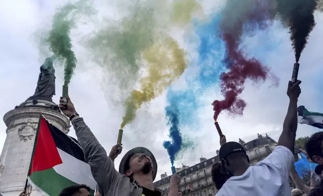 Protesters release smoke in the colors of the Olympic rings during a demonstration by several associations for what they called the "Counter Opening Ceremony" on Republique plaza against the 2024 Summer Olympics, Thursday, July 25, 2024, in Paris, France. Demonstrators gave speeches about the cost of the Olympic Games and said authorities have been using the Games as a pretext for what they call social cleansing, by removing migrants and homeless people off the streets in order to preserve a picture-postcard image of the city for the millions of visitors coming. (AP Photo/David Goldman)