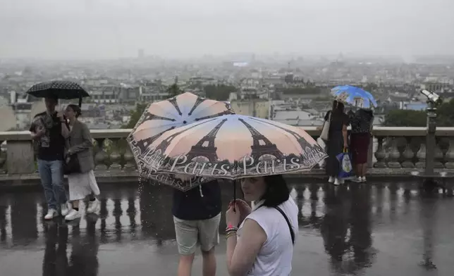 People in the Montmartre district use umbrellas to protect from the rain in Paris, France, during the opening ceremony of the 2024 Summer Olympics, Friday, July 26, 2024. (AP Photo/Dita Alangkara)