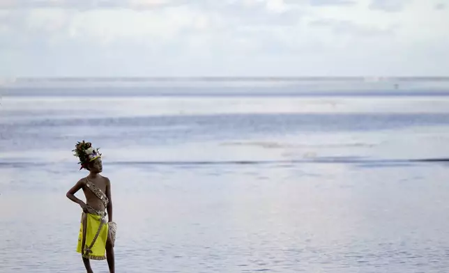 A young dancer waits along the beach before an opening ceremony for the 2024 Summer Olympics surfing competition Friday, July 26, 2024, in Papara, Tahiti. (AP Photo/Gregory Bull)