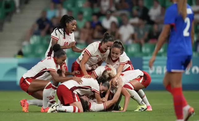 Canada's players celebrate after Vanessa Gille, bottom center, scored her side's second goal during the women's Group A soccer match between Canada and France at Geoffroy-Guichard stadium during the 2024 Summer Olympics, Sunday, July 28, 2024, in Saint-Etienne, France. (AP Photo/Silvia Izquierdo)