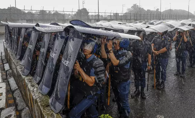 Police personnel use shields as cover during rainfall along the main road leading to the House of Representatives ahead of the third State of the Nation Address by Philippine President Ferdinand Marcos Jr. in Quezon City, Philippines, Monday, July 22, 2024. (AP Photo/Mark Cristino)